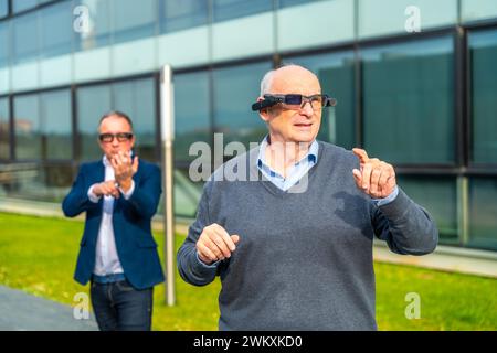 Homme d'affaires expérimentant avec casque à vision mixte augmentée dans un parc urbain à côté d'un bâtiment financier Banque D'Images