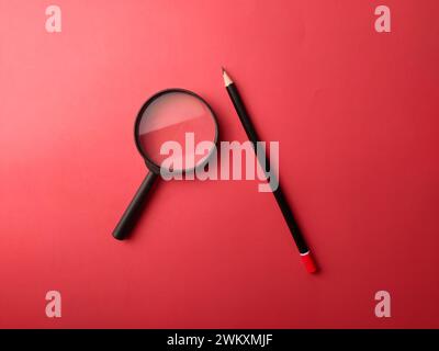 Crayon vue de dessus et loupe sur fond rouge Banque D'Images