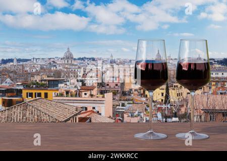 Deux verres de vin rouge sur la table face à la vue de Rome avec un ciel bleu, mettant en valeur la majestueuse skyline de la ville. Banque D'Images