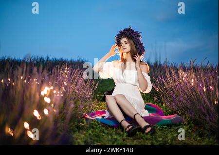Ivano-Frankivsk, Ukraine 28 juillet 2023 : la jeune fille est assise sur l'herbe entre les rangées de lavande, les buissons de lavande et les fleurs sont illuminés par le grenier Banque D'Images