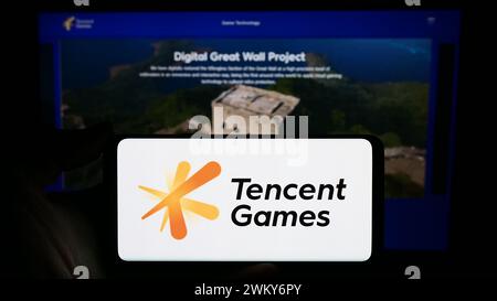 Personne tenant un smartphone avec le logo de la société chinoise de jeux vidéo Tencent Games en face du site Web. Concentrez-vous sur l'affichage du téléphone. Banque D'Images