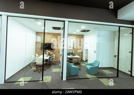 La personne est immergée dans une tâche dans un bureau élégant avec des murs de verre transparents. Le design moderne comprend la brique apparente, un moniteur élégant, confortable Banque D'Images