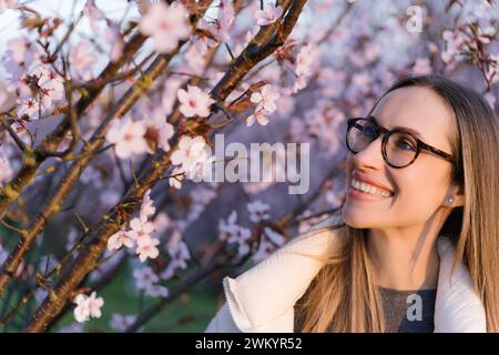 Femme joyeuse dans des verres appréciant les fleurs de cerisier dans le parc au printemps Banque D'Images