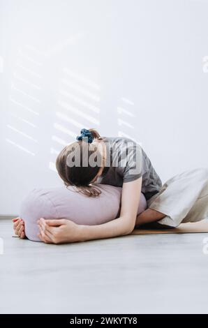 Femme dans des vêtements décontractés pratiquant la pose papillon yin yoga avec traversin Banque D'Images