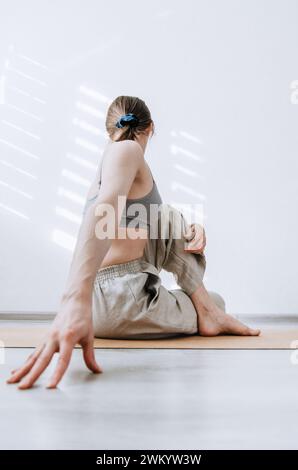 Femme dans un pantalon en lin naturel faisant une pose de yoga twist assis sur un tapis de liège Banque D'Images