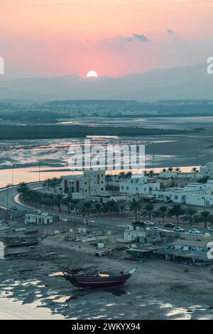 Coucher de soleil dans la ville de sur. Vue sur la partie ouest de la ville sur. Facteur dhow en distance. Sur, Oman Banque D'Images