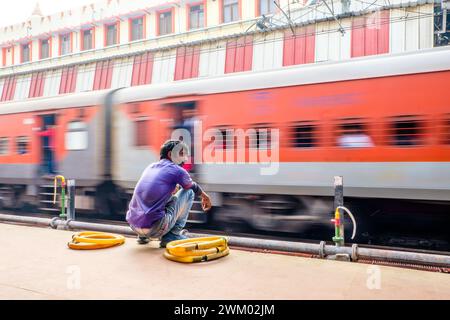 Un employé des chemins de fer indiens attendant sur un quai pendant le passage d'un train Banque D'Images