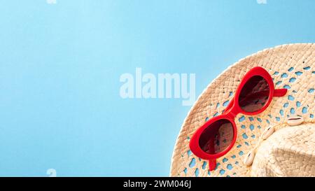 Chapeau de paille avec lunettes de soleil rouges sur un fond bleu en été Banque D'Images