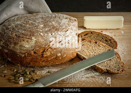 Pâte de levain crue sur une planche de bois avec des graines de citrouille et des ustensiles de cuisine Banque D'Images