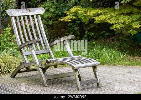 Papillon virgule reposant sur une vieille chaise de vapeur sur une terrasse en bois près d'une parcelle d'herbe dans une zone de jardin laissée à l'état sauvage avec un hochet jaune Banque D'Images