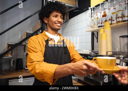 Jeune barista souriant servant du café au client au café Banque D'Images