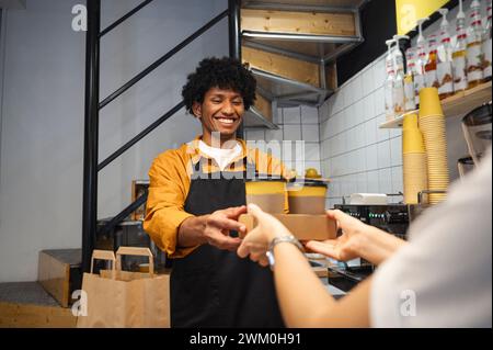 Le barista souriant remet des tasses à emporter au client au café Banque D'Images