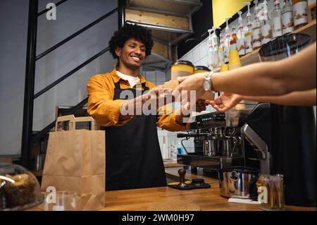 Barista heureux de remettre le plateau à emporter au client au comptoir du café Banque D'Images