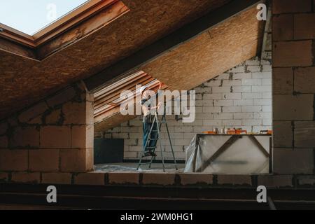 Ouvrier de la construction debout sur une échelle et travaillant dans une chambre en rénovation Banque D'Images