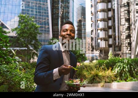 Heureux homme d'affaires mature assis avec bol de salade au parc de bureau Banque D'Images