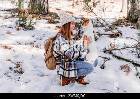 Femme souriante accroupie avec un chien sur la neige en hiver Banque D'Images