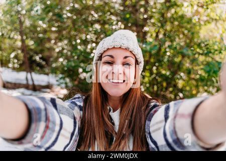 Femme heureuse portant un bonnet en tricot et prenant selfie Banque D'Images