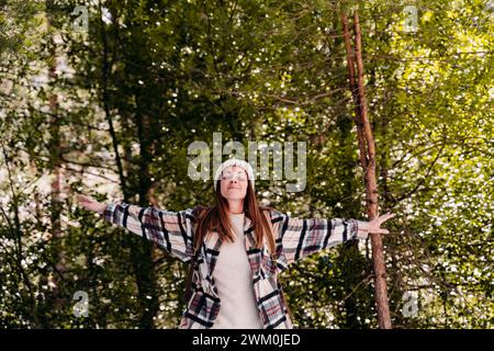 Femme insouciante debout avec les bras tendus au milieu des arbres dans la forêt Banque D'Images