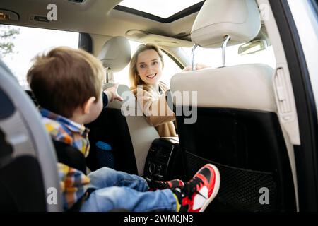 Femme souriante regardant son fils assis sur le siège arrière de la voiture Banque D'Images