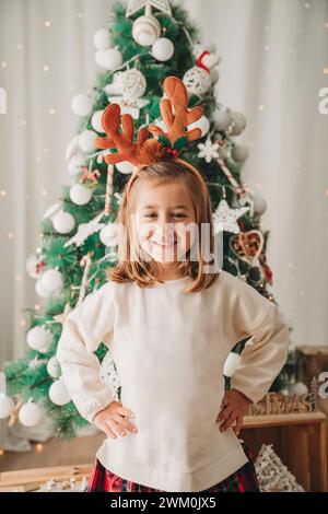 Fille heureuse debout avec les mains sur la hanche devant l'arbre de Noël Banque D'Images