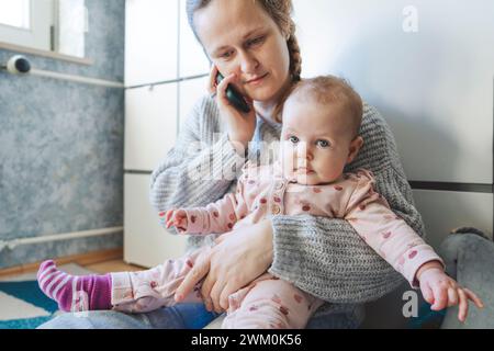 Bébé fille avec mère parlant sur téléphone intelligent à la maison Banque D'Images