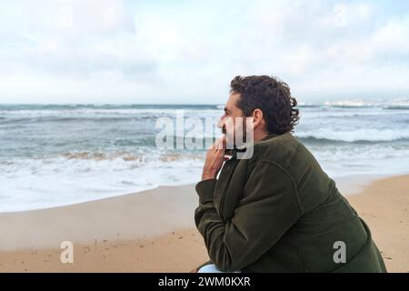 Homme accroupi devant la mer à la plage Banque D'Images