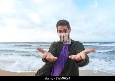 Homme souriant atteignant les mains en face de la mer à la plage Banque D'Images