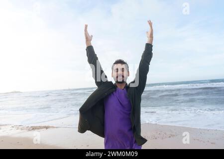 Homme insouciant debout avec les bras levés devant la mer à la plage Banque D'Images