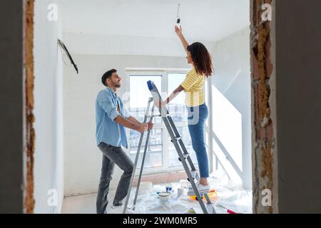 Jeune homme aidant la femme à installer l'ampoule à la nouvelle maison Banque D'Images