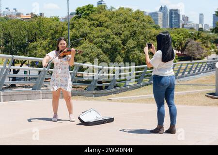 Femme touriste debout à l'extérieur prenant des photos avec son téléphone de violoniste vénézuélien Latina busker à Buenos Aires travaillant à faire de la musique, de la musique et du peop Banque D'Images