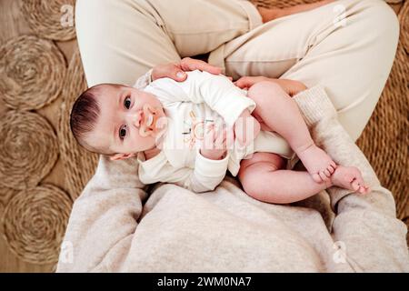 Bébé fille suçant la sucette dans les bras de la mère à la maison Banque D'Images