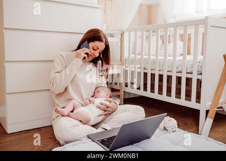 Freelance tenant bébé fille et parlant sur téléphone portable au bureau à domicile Banque D'Images