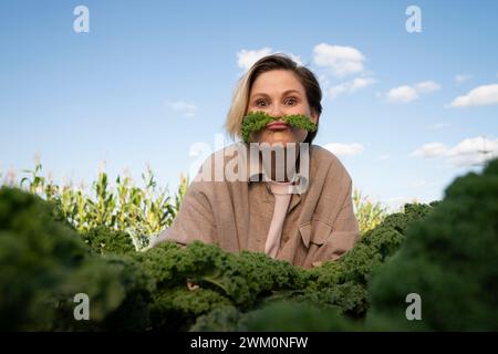 Fermier ludique avec des feuilles de chou frisé sur les lèvres à la ferme Banque D'Images