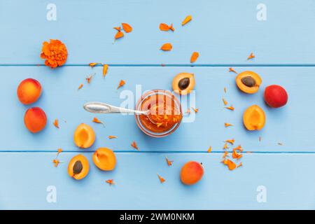 Confiture d'abricots maison avec pétales de souci et abricots crus sur bois bleu Banque D'Images