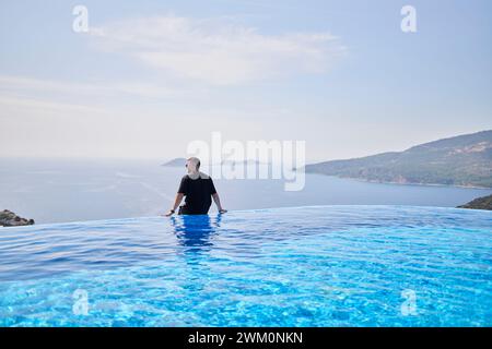 Homme regardant la mer assis sur le bord de la piscine à la villa Banque D'Images