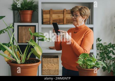 Femme senior prenant photo de la plante par téléphone intelligent à la maison Banque D'Images