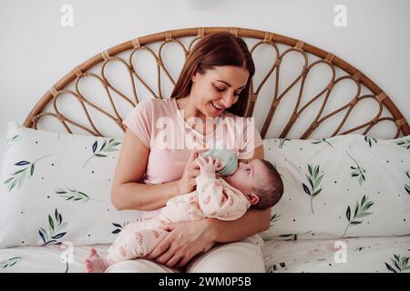 Mère souriante donnant du lait à sa fille sur le lit à la maison Banque D'Images