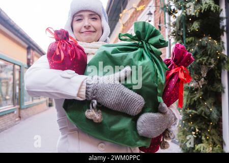 Femme souriante portant des sacs cadeaux dans la rue à Noël Banque D'Images