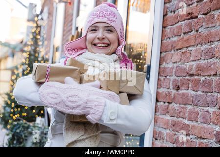 Femme heureuse portant des boîtes-cadeaux près du mur de briques à Noël Banque D'Images