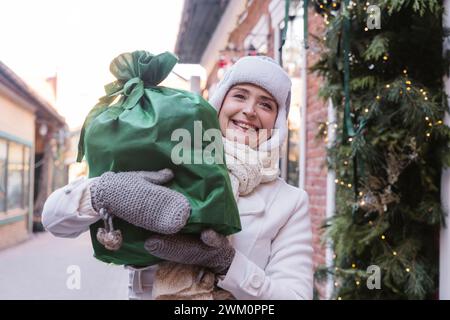 Femme heureuse portant un sac cadeau vert dans la rue à Noël Banque D'Images