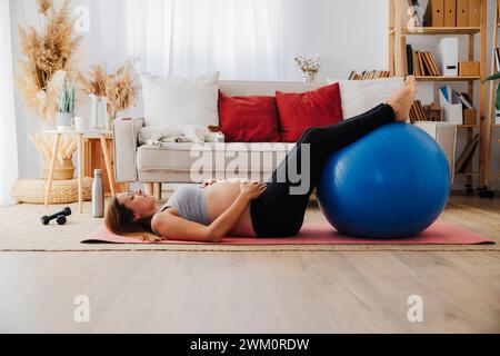 Femme enceinte allongée sur un tapis de yoga avec ballon de fitness à la maison Banque D'Images