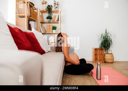 Femme enceinte avec les mains sur le ventre assis à la maison Banque D'Images