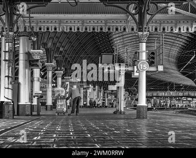 Une plate-forme de gare, bordée de colonnes, courbes, dans un hall principal. Une canopée historique du XIXe siècle est au-dessus et un nettoyeur vide les ordures Banque D'Images