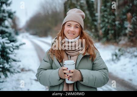 Femme souriante portant des vêtements chauds et tenant thermos Banque D'Images