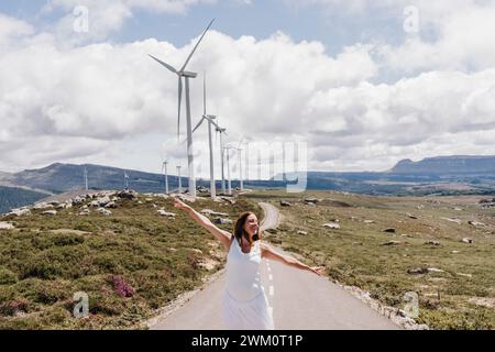 Espagne, Madrid, femme enceinte debout avec les bras levés au milieu de la route s'étendant devant le parc éolien Banque D'Images