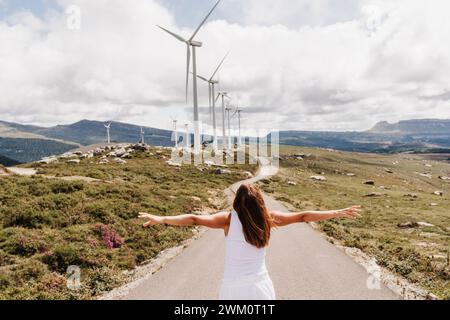 Espagne, Madrid, dos de femme debout avec les bras levés au milieu de la route s'étendant devant le parc éolien Banque D'Images