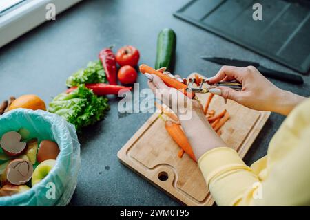 Mains de jeune femme épluchant la carotte dans la cuisine à la maison Banque D'Images