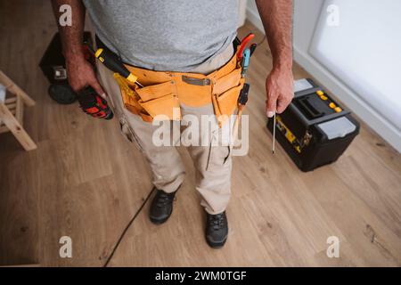 Réparateur portant la ceinture à outils et debout à la maison Banque D'Images