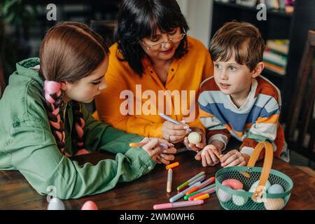 Heureuse grand-mère avec petits-enfants peignant des œufs de Pâques Banque D'Images