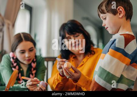 Garçon souriant avec sœur et grand-mère peignant des œufs de Pâques Banque D'Images